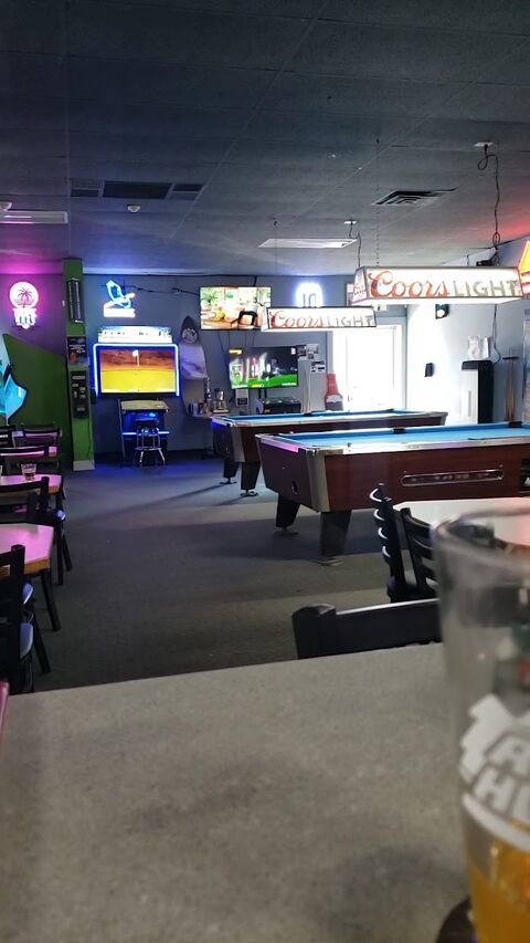 The back room at Just Chill under neon: two pool tables with blue felt, a Golden Tee arcade cabinet and Coors Light lamps overhead.